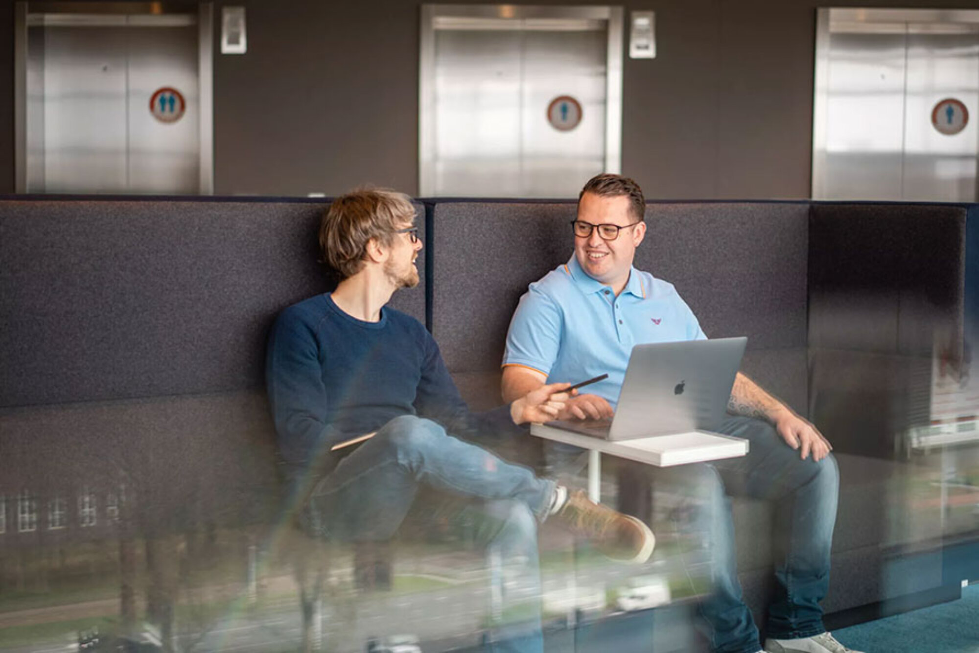 Twee mannen die een ontspannen meeting hebben omdat zij hun werkstress verminderen door gebruik te maken Clientbox. Terwijl zij een meeting hebben pakken hun collega's vragen van klanten op die normaal zouden blijven liggen totdat zij klaar zijn met de meeting.